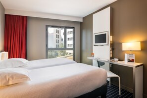 Habitación de hotel con cama, escritorio, televisor y ventana con vistas a edificios.