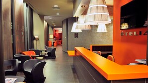 Zona de recepción de hotel con diseño moderno, que incluye un mostrador de recepción, área de descanso con sillas y un televisor grande montado en la pared.