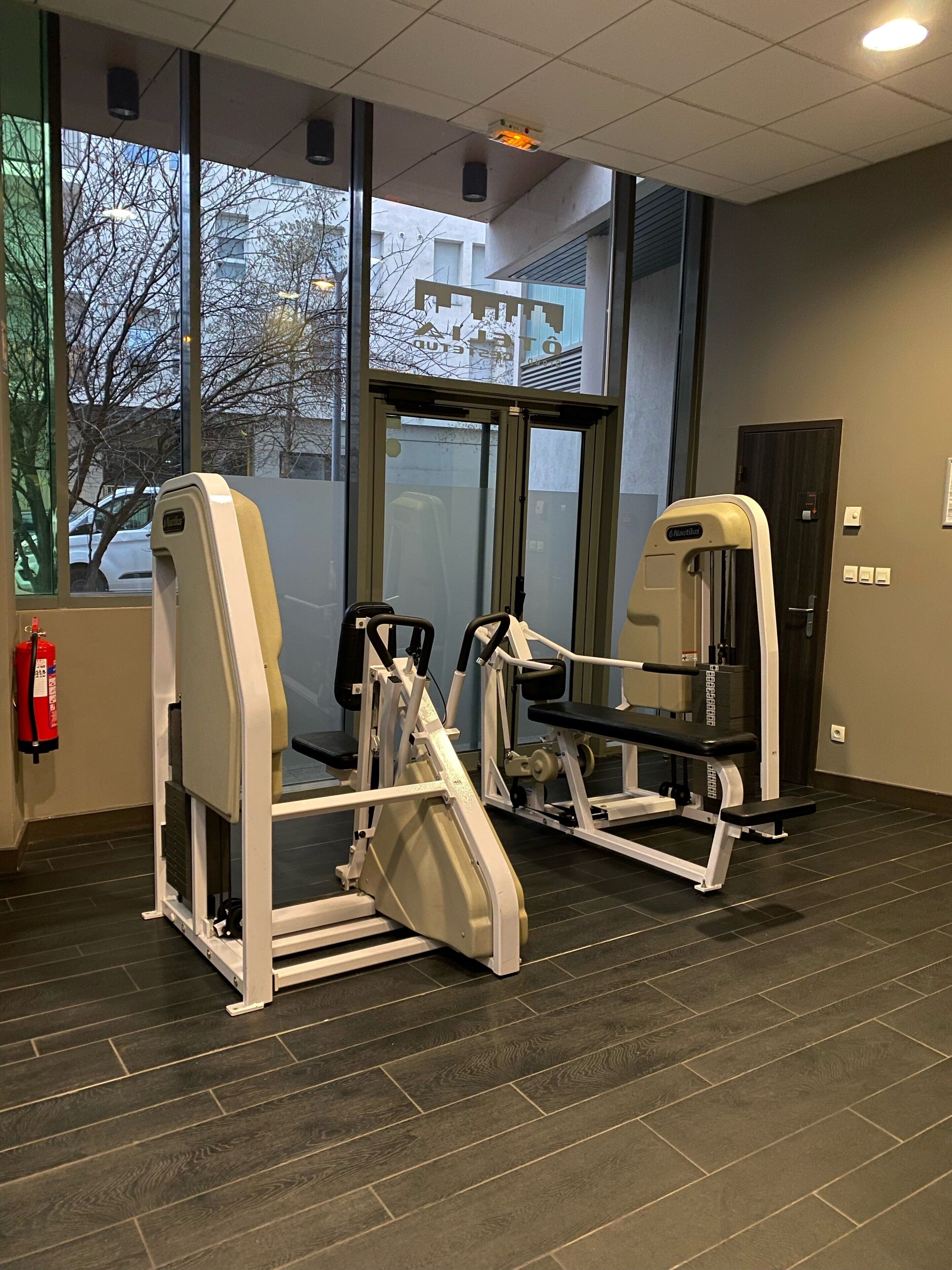 Un gimnasio con dos máquinas de ejercicio, un extintor y una puerta con un cartel en la parte superior.