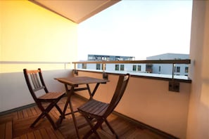Un balcón con una mesa de madera y dos sillas, con vistas a un edificio con varias ventanas.