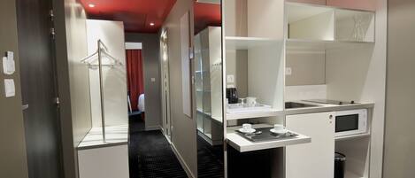 A modern hotel room with a kitchenette, a walk-in closet, and a shower area.