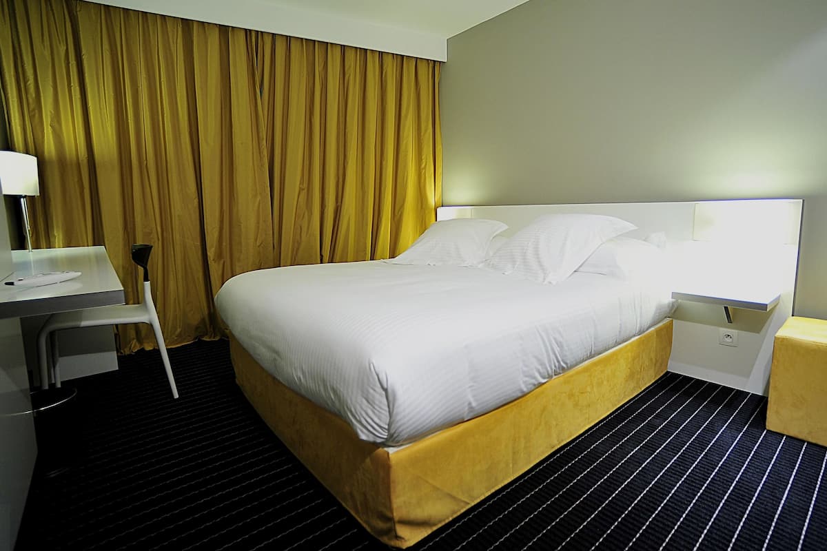 Una habitación de hotel con cama, escritorio, silla y mesita de noche.