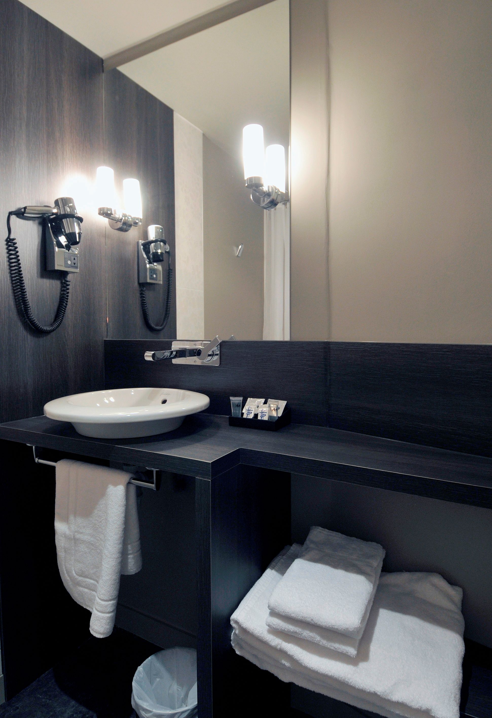 A modern bathroom with a large mirror, a sink, and two towel racks with folded towels.