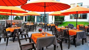 Un área de comedor al aire libre con mesas y sillas, cubierta por sombrillas grandes.