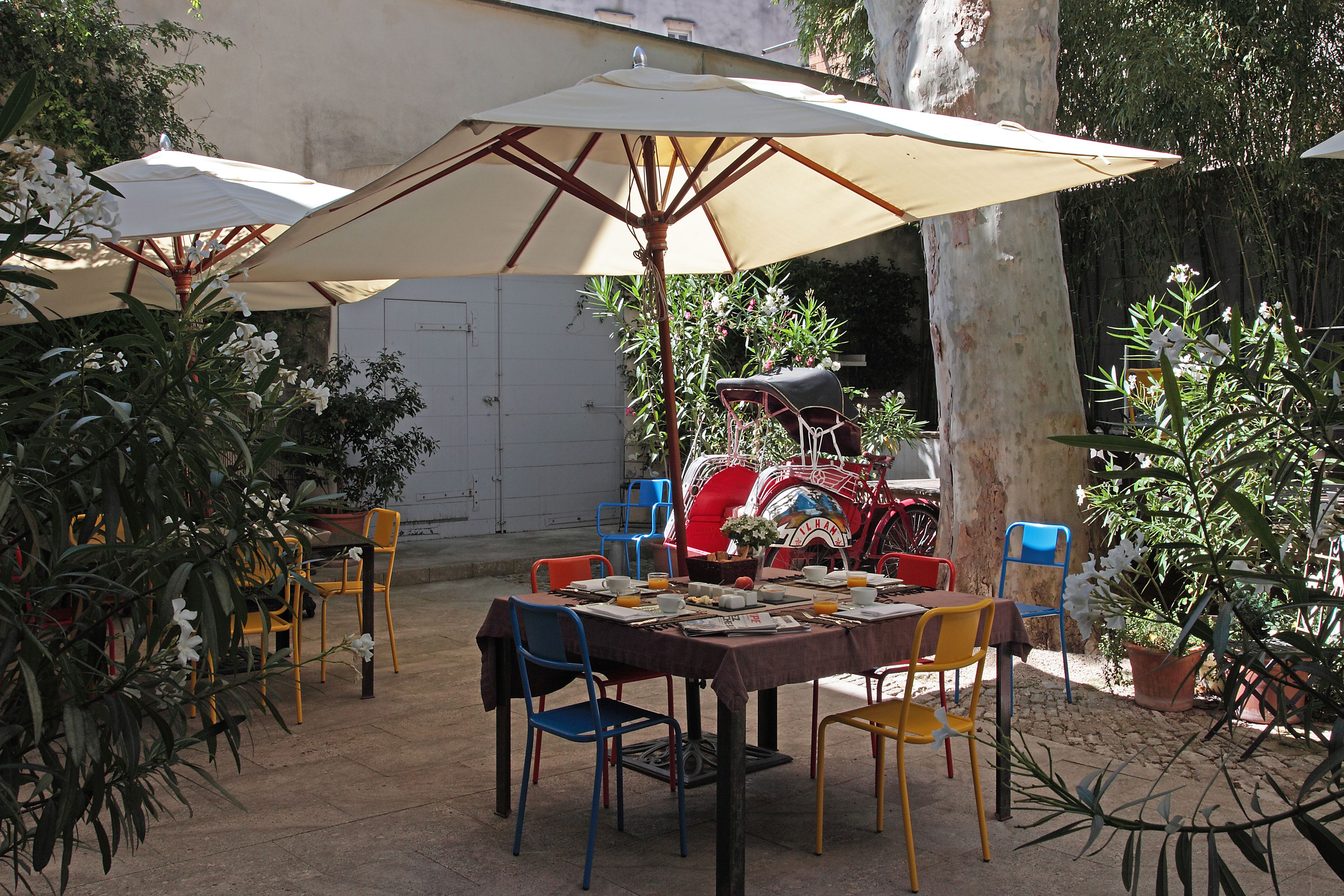 Un área de comedor al aire libre con una mesa para dos, rodeada de sillas y cubierta por una sombrilla grande.