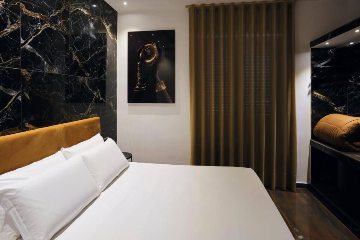 Una camera d'albergo con un letto, una testiera, un'opera d'arte appesa al muro e una finestra con tende.