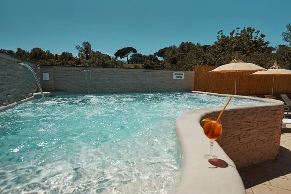 Una piscina con agua cristalina, un muro de piedra y una bebida en una silla de descanso.