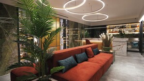 Um interior moderno com um sofá vermelho, uma planta grande e um espaço bar com garrafas.