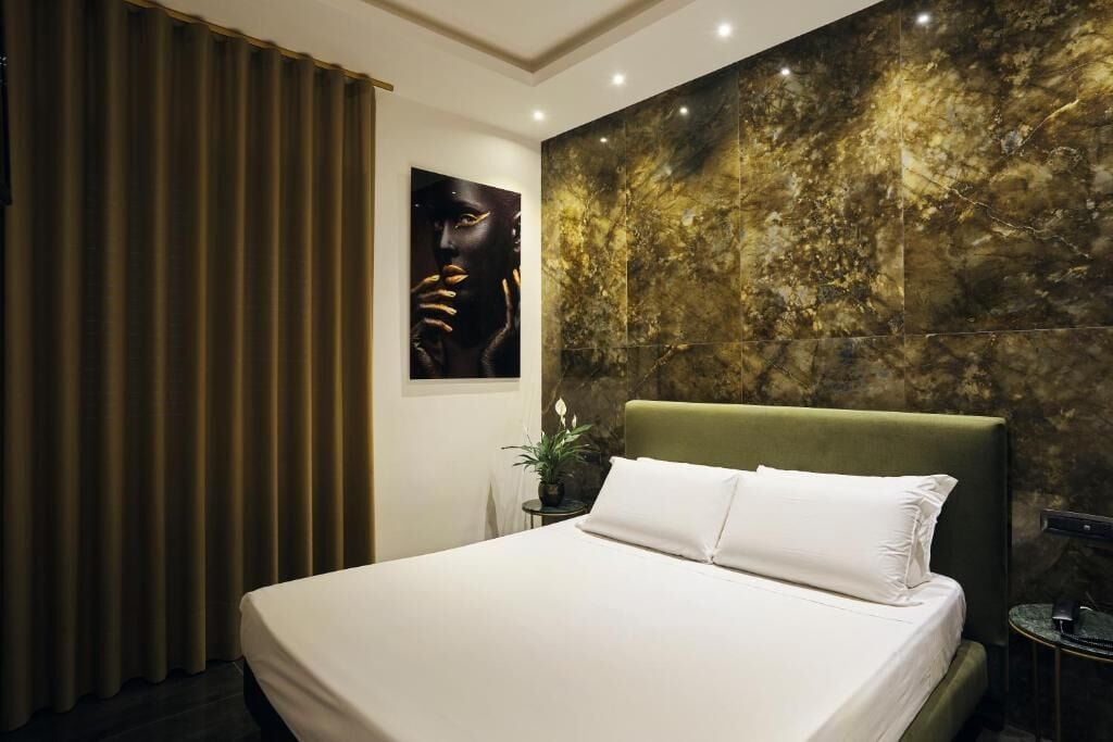 Un dormitorio con una cama grande, un cabecero, una pared con textura que simula mármol, una cortina y una obra de arte enmarcada.