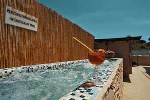 Una piscina de hidroterapia con un cartel que dice "PERCORSO IDROTHERAPICO HYDROTHERAPY POOL" y un vaso de bebida con una pajita en el borde de la piscina.