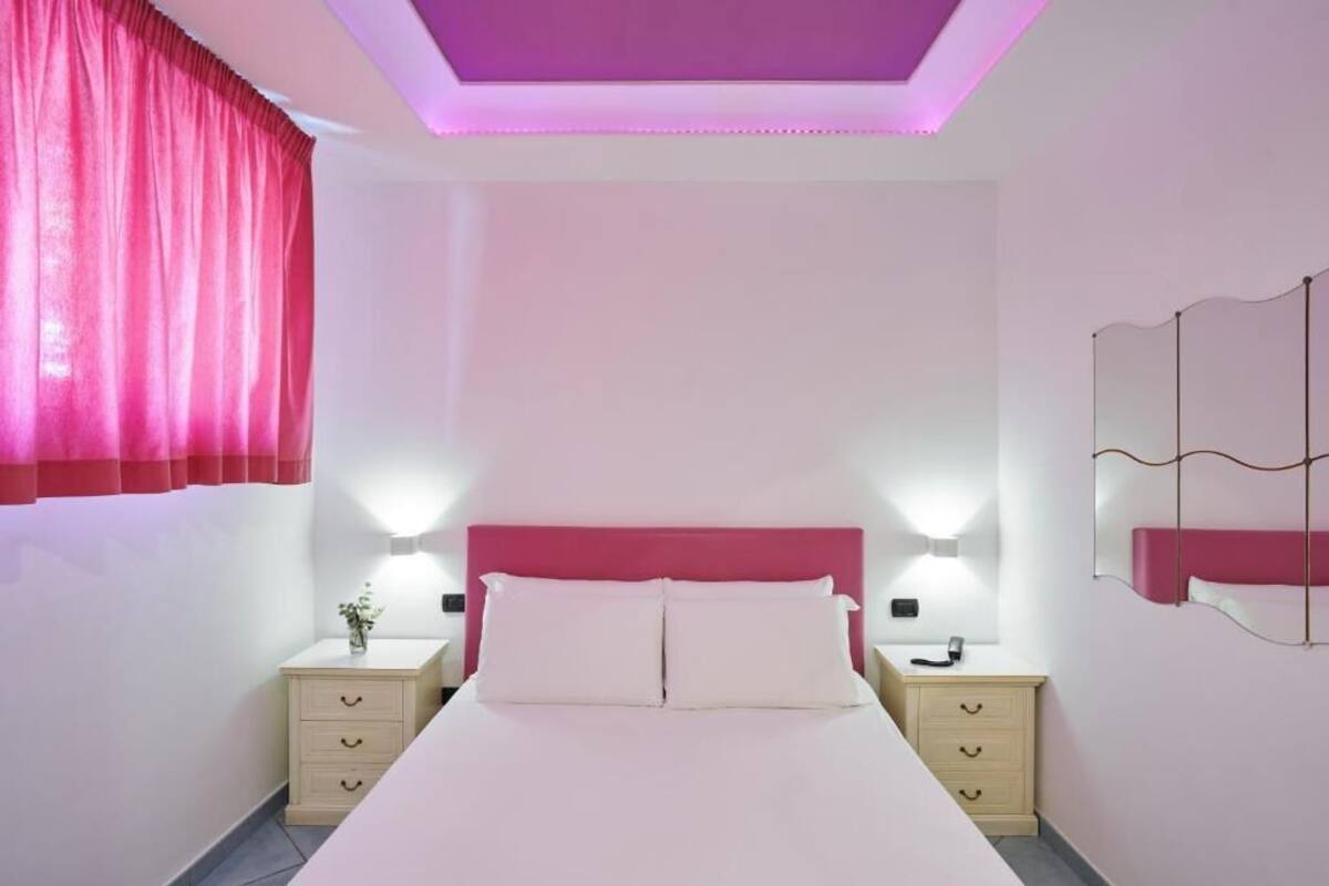 Una camera da letto con un letto, comodini, uno specchio e una finestra con tende.