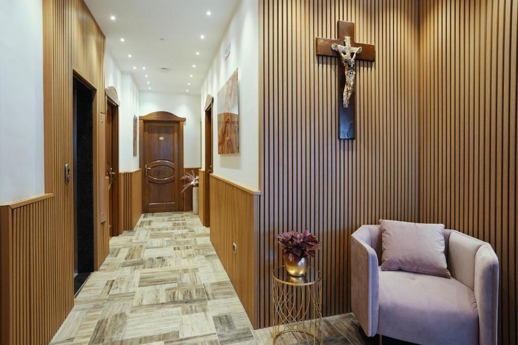 A hallway with wooden paneling, a cross on the wall, and a seating area with a vase of flowers.
