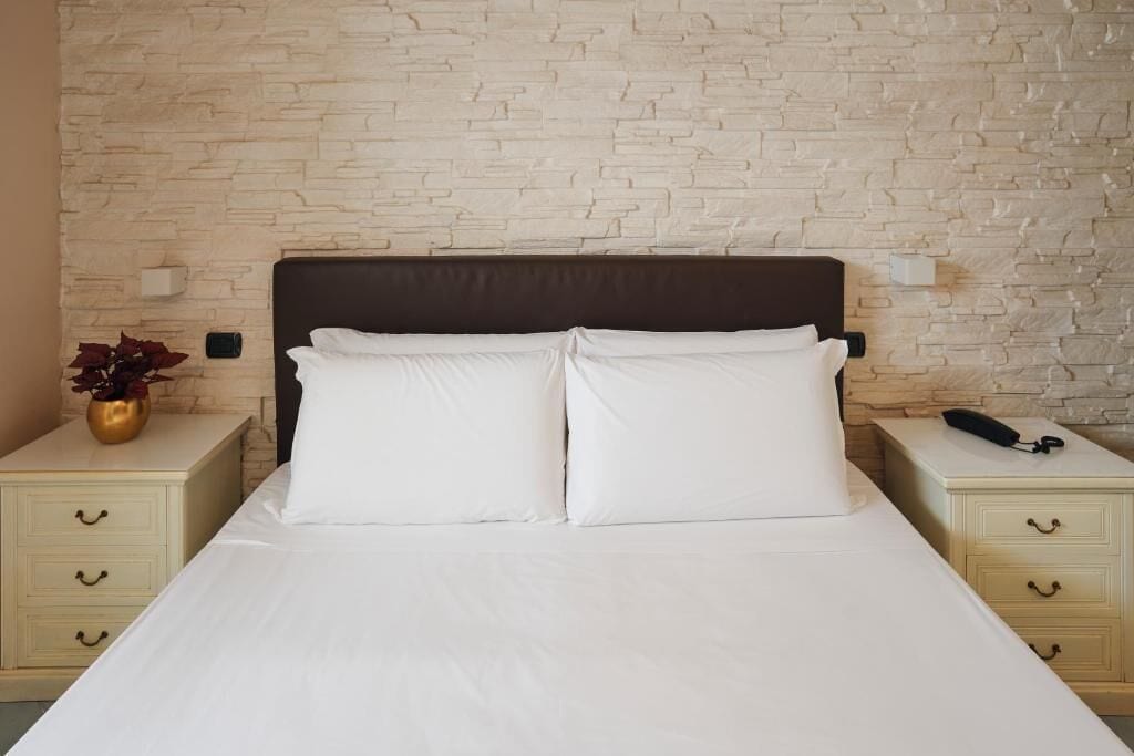Un lit avec du linge de lit blanc, une tête de lit sombre et deux tables de chevet dotées de tiroirs.