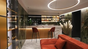 Uma área de bar moderna com bancada de mármore, dois banquetas e um sofá vermelho em primeiro plano.