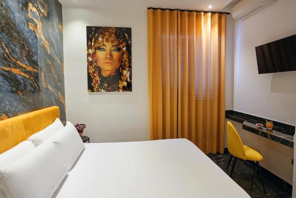 A hotel room with a bed, a painting on the wall, a TV, and a window with curtains.