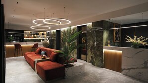 Um lobby de hotel moderno com um sofá vermelho, área de bar e balcão de recepção.