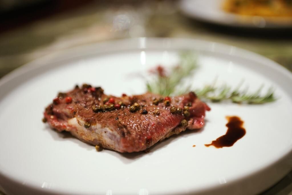 A plate with a piece of meat, possibly steak, garnished with herbs and a sauce.