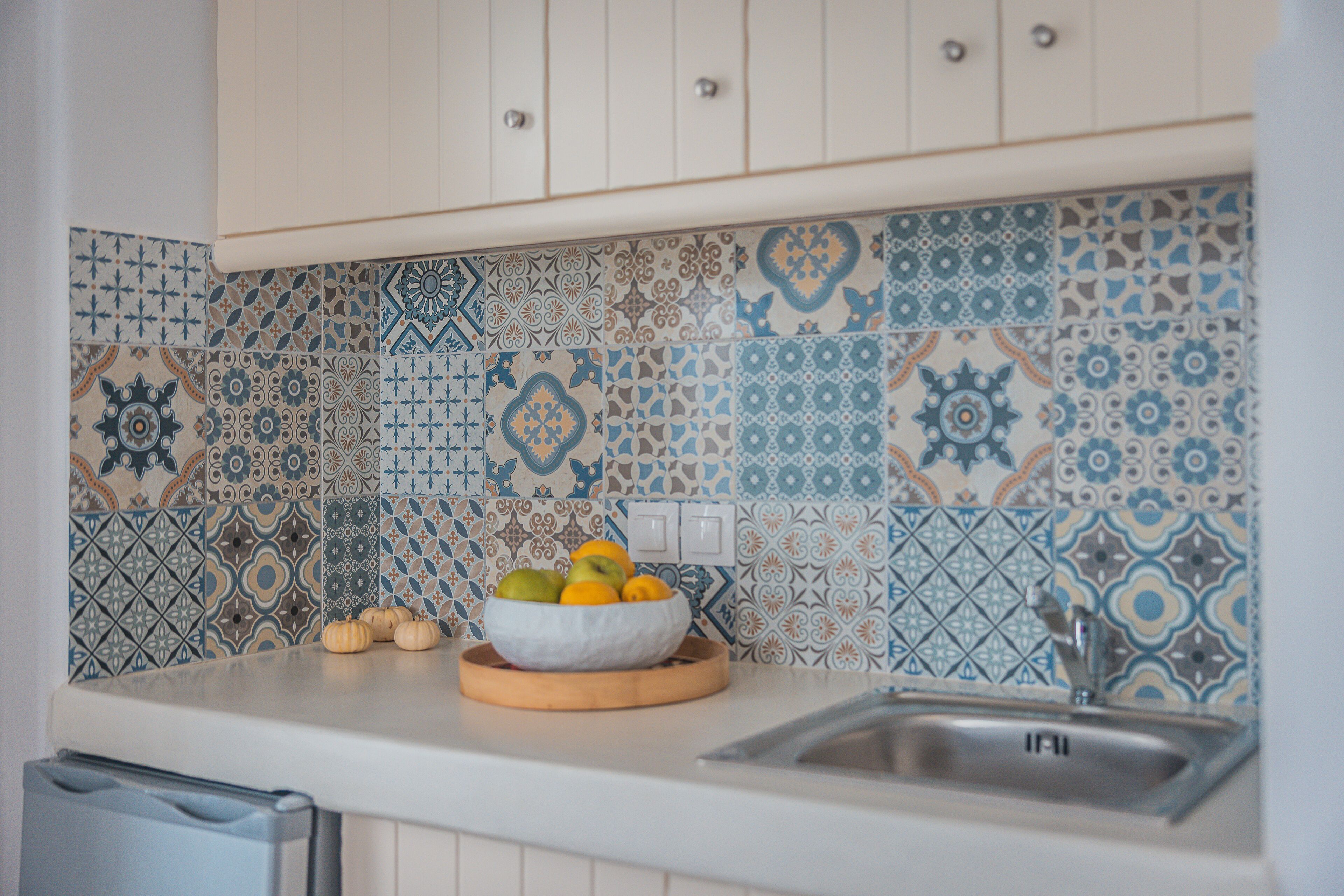 Une cuisine avec des carreaux décoratifs, un panier de fruits sur le comptoir et un évier.