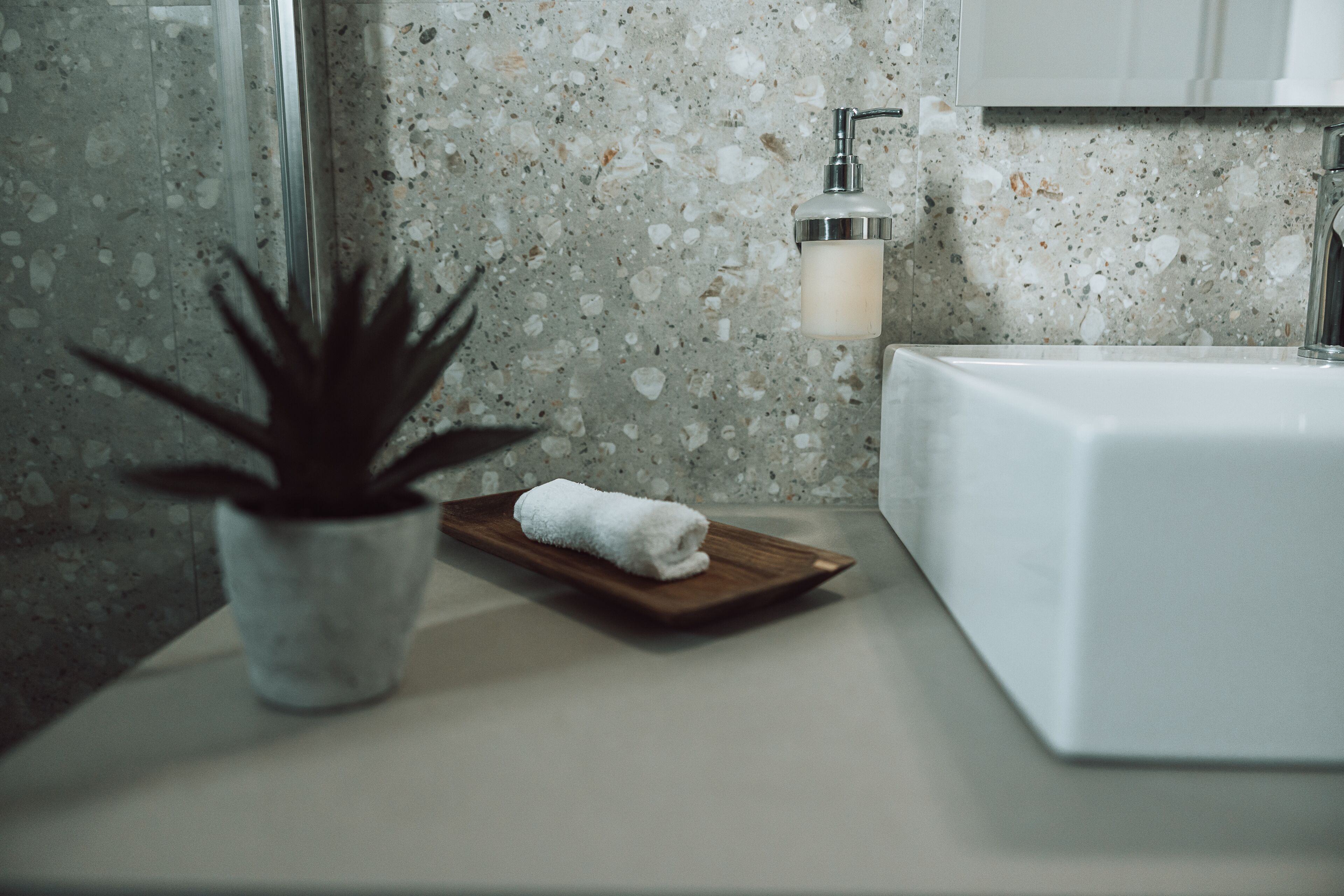 Un baño con un lavamanos blanco, una planta en maceta y una toalla sobre una bandeja de madera.