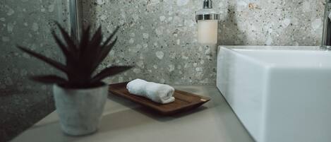 A bathroom with a white sink, a potted plant, and a towel on a wooden tray.