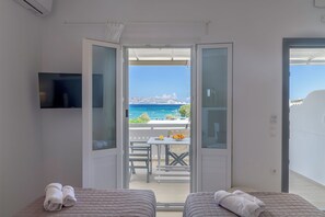 A room with two beds, a TV, and a balcony with a table and chairs. - En Milo (Milos)