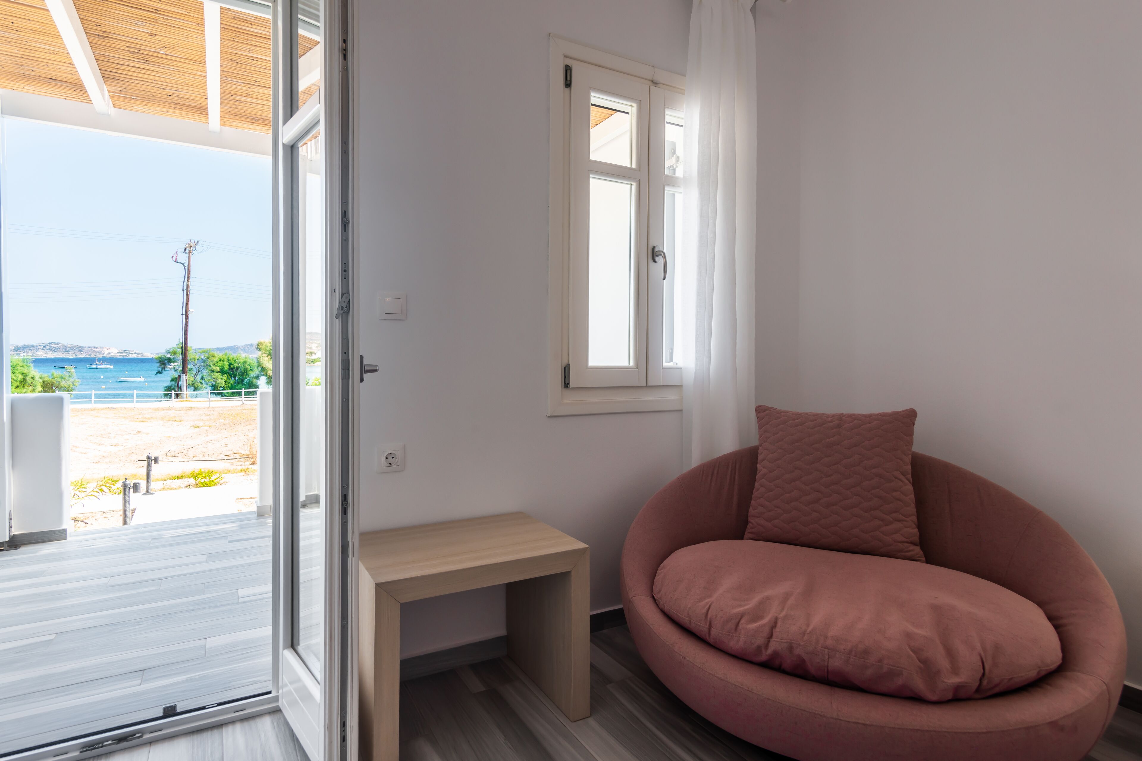 Una habitación con vista al mar, piso de madera, una silla rosa y una mesita.