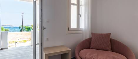 Una habitación con vista al mar, piso de madera, una silla rosa y una mesita.
