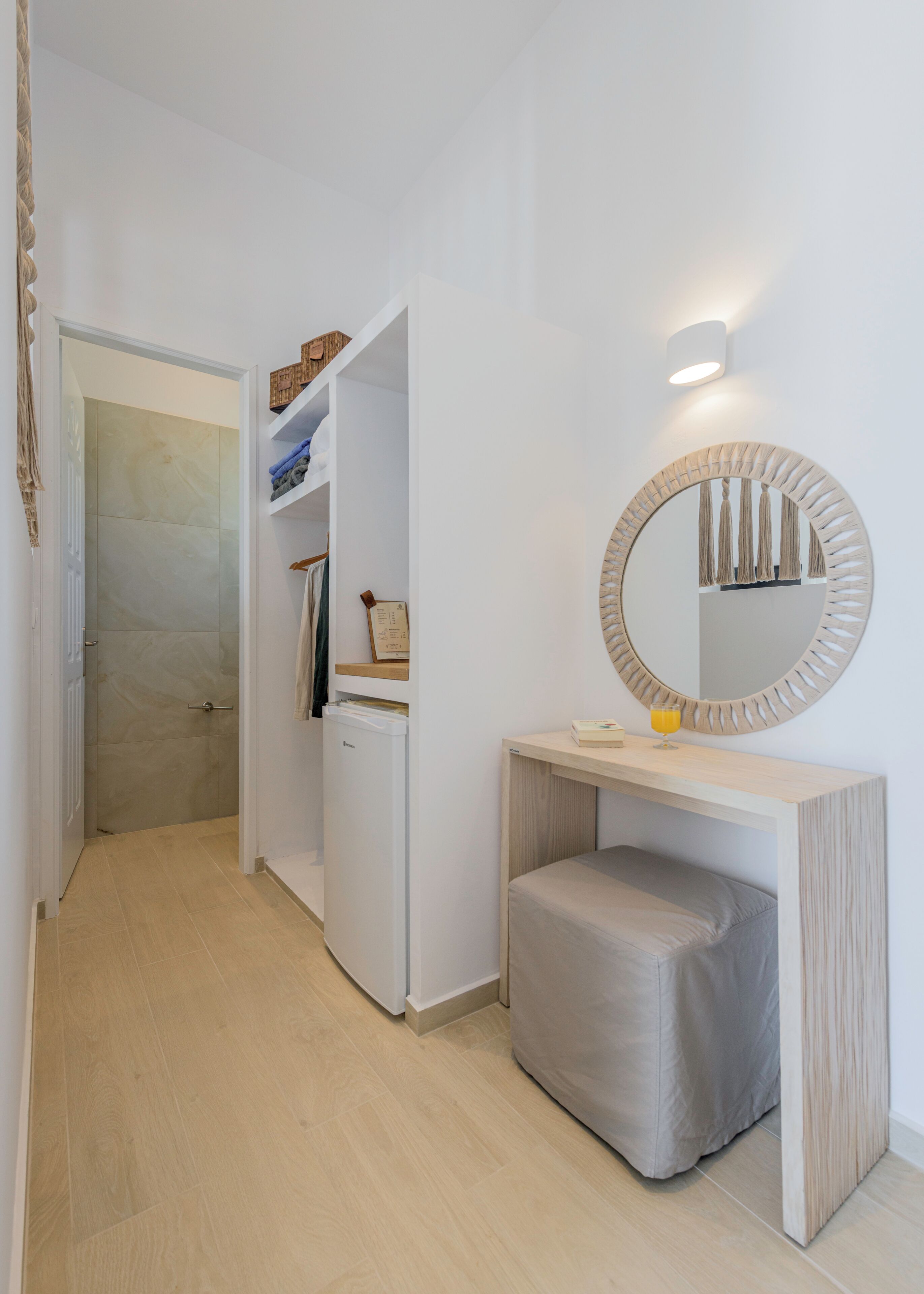 A hallway with a white door leading to a bathroom, a vanity with a mirror, and a small bench.