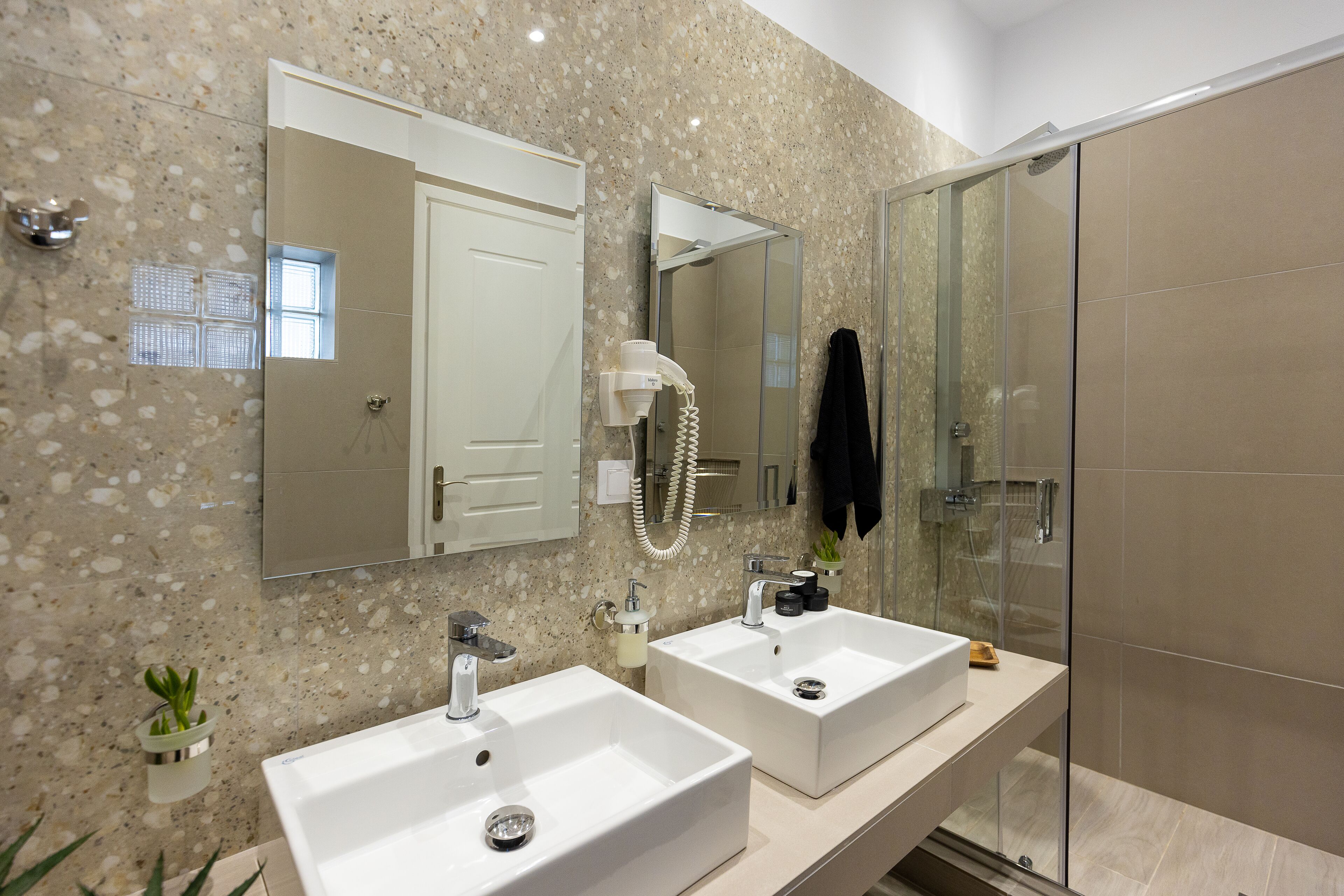 Un baño moderno con dos lavamanos, cabina de ducha con mampara de vidrio y salpicadero de mármol.