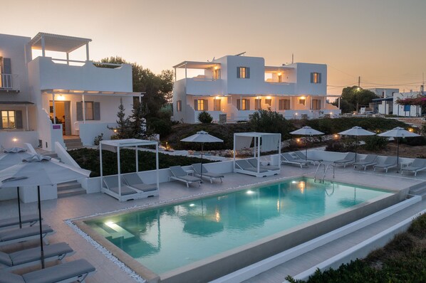 A modern hotel with a swimming pool, sun loungers, and a covered seating area. - En Milo (Milos)