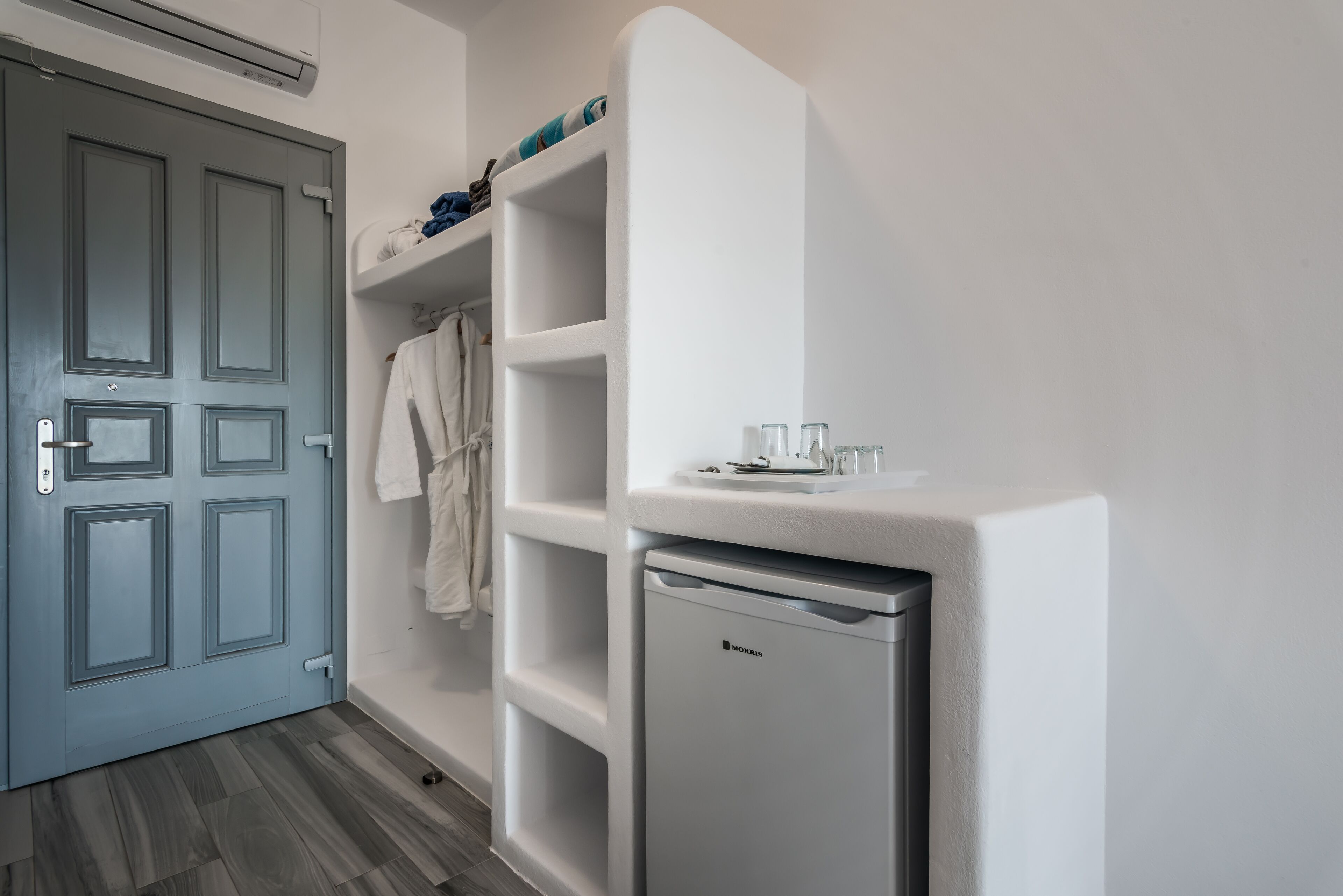 A compact bathroom with a grey door, a white towel rack, and a small white shelf with toiletries.