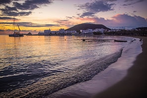 A coastal scene with a sailboat, calm waters, and buildings along the shore. - En Milo (Milos)