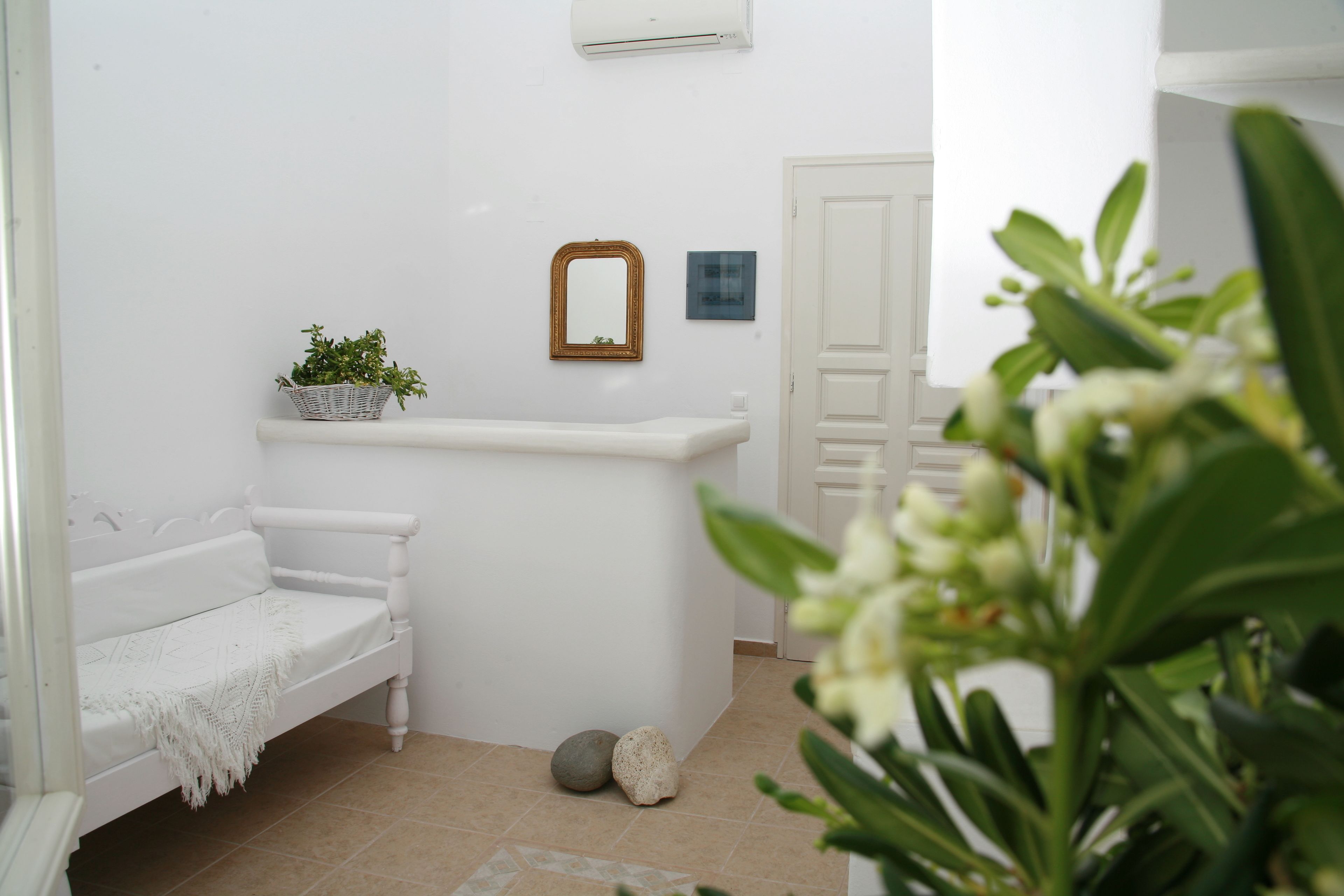 Een witte badkamer met een bankje, een plantje, een spiegel en een deur.