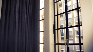 A room with a large window featuring a black metal grid, a dark curtain, and a view of a multi-story building with balconies. - Galeón Mar del Plata (Mar del Plata)