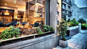 A modern hotel with a large window displaying a cozy seating area with chairs and a table, surrounded by greenery and a view of a cityscape. - Galeón Mar del Plata (Mar del Plata)