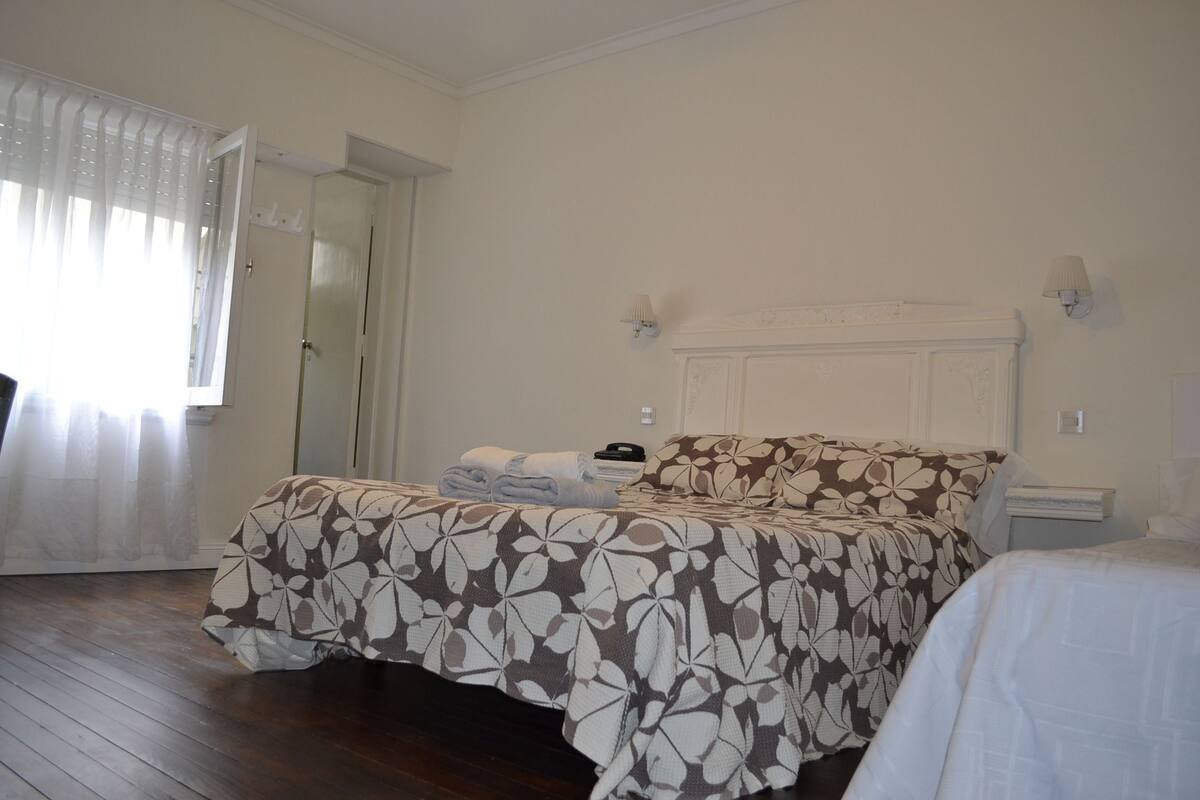 A hotel room with a double bed, a bedside table, a nightstand, and a window with curtains.