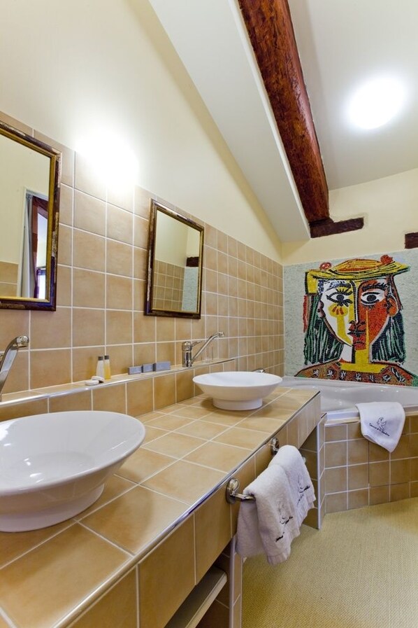 Ein Badezimmer mit zwei Waschbecken, einem Spiegel und einer gefliesten Wand mit einem farbenfrohen Wandgemälde.