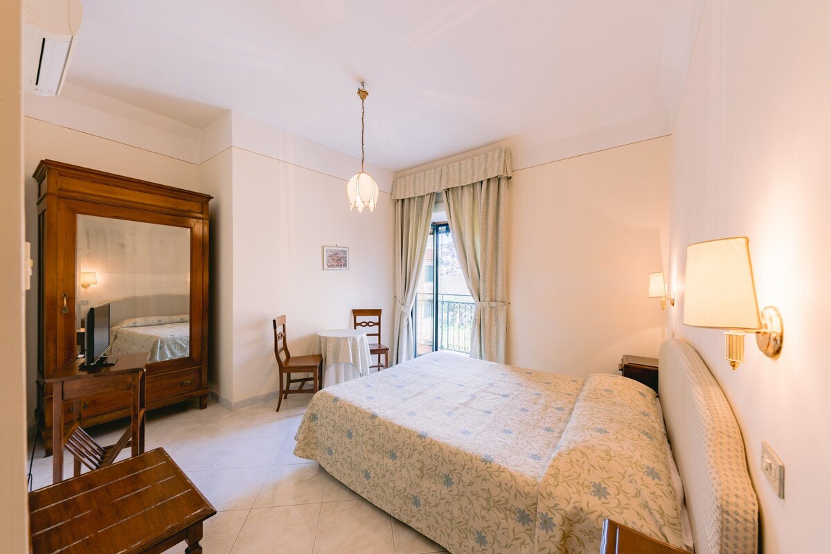 Un dormitorio con cama, escritorio, silla, cómoda y ventana con cortinas.