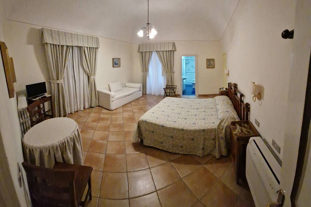A bedroom with a bed, a sofa, a TV, and a bathroom visible through an open door.