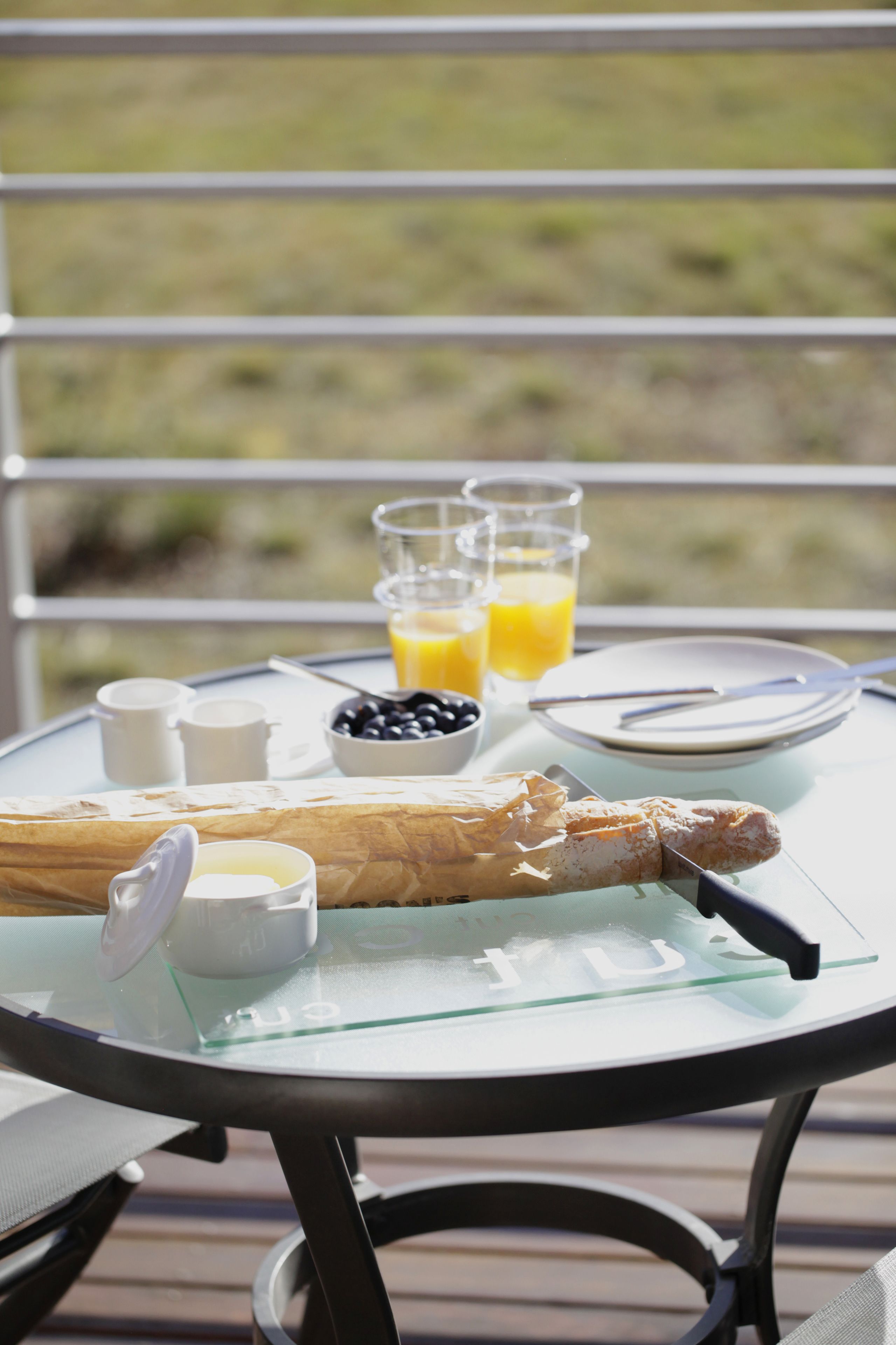 A breakfast table with a croissant, a bottle of juice, a bowl of blueberries, and a glass of orange juice.