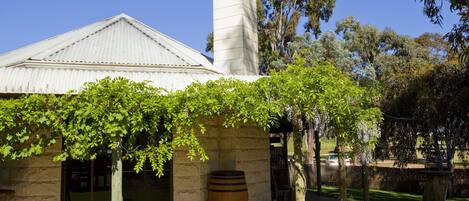 Un edificio con fachada de piedra, un barril de madera grande y una pérgola cubierta de hiedra.