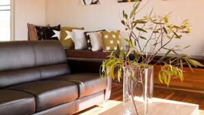 A modern living room with a leather sofa, a wooden coffee table, and a vase with branches. There are wall art pieces and a sofa with star-patterned pillows. - Eco-luxe at Mount Avoca (Percydale)