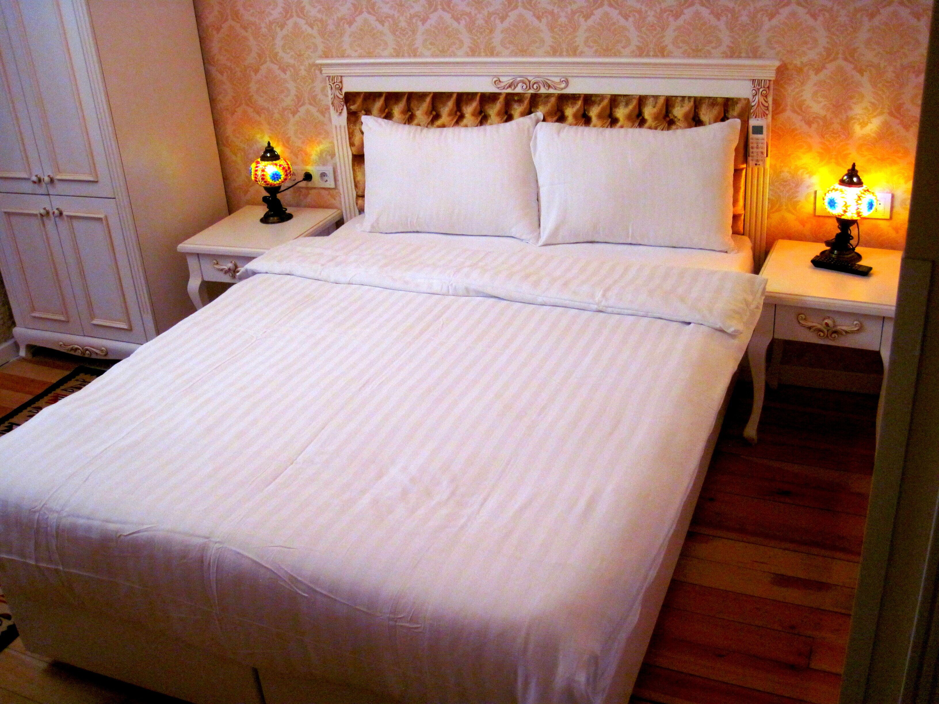 A neatly made bed with white linens, two bedside tables with lamps, and a wooden floor.