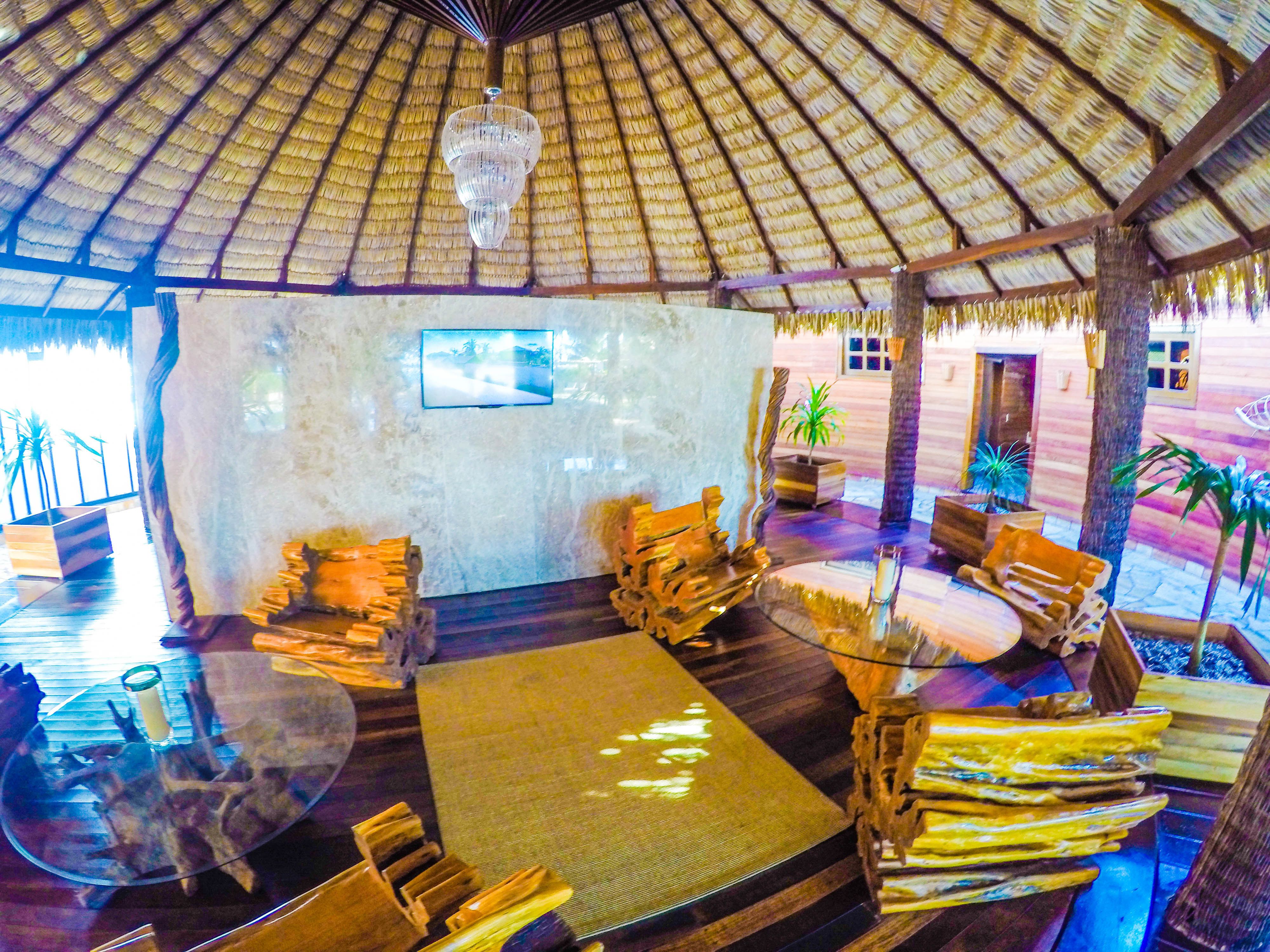 A thatched-roof lounge area with wooden furniture and a glass table.