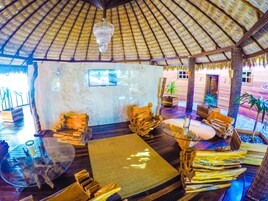 A thatched-roof lounge area with wooden furniture and a glass table.