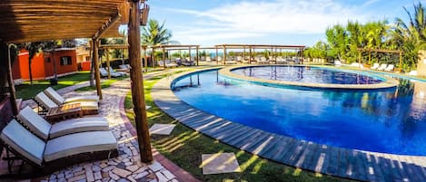 Una piscina con sillas de descanso y una pérgola, rodeada de palmeras y un sendero de piedra.