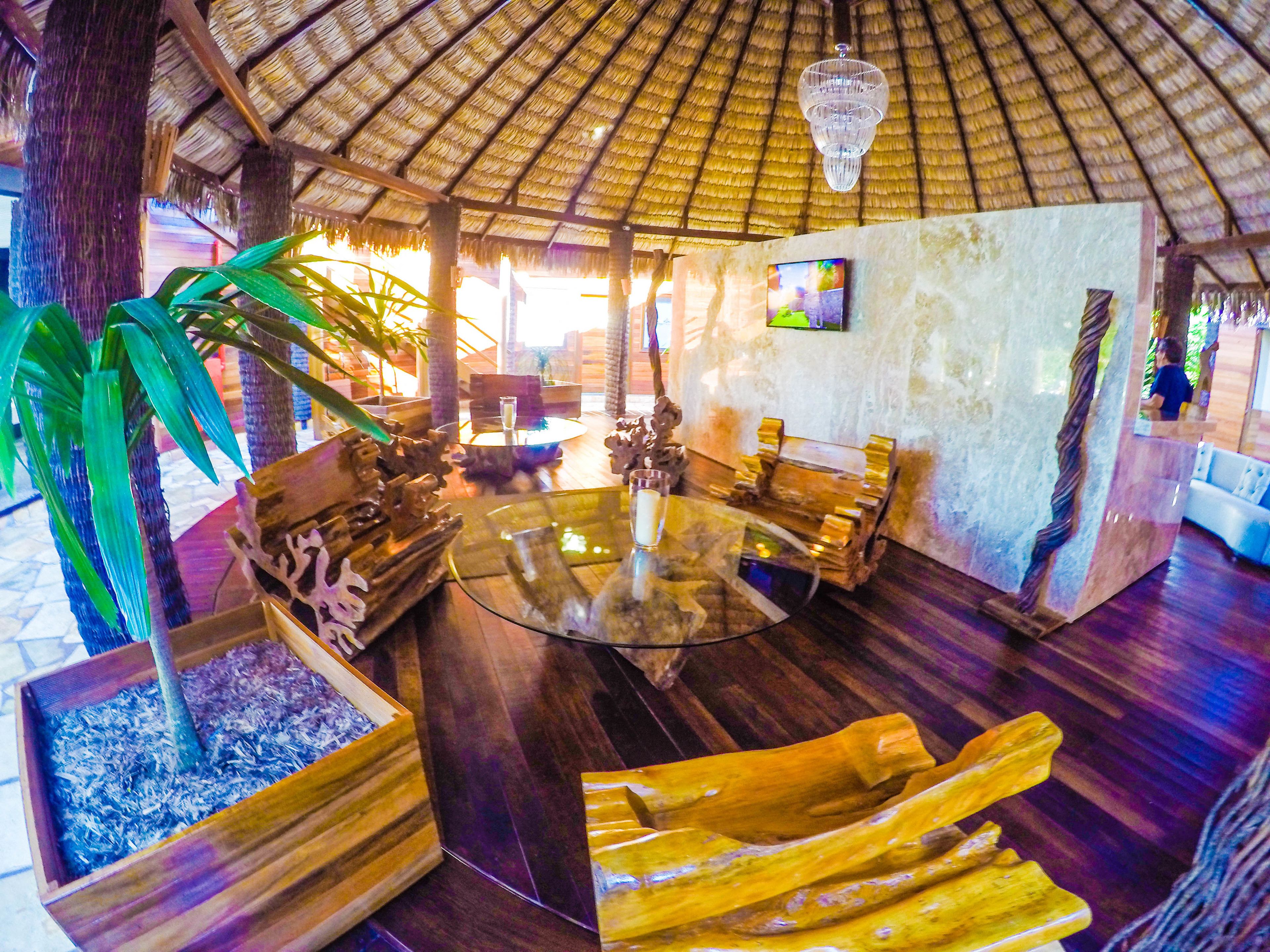 Habitación de estilo tropical con techo de paja, muebles de madera y una mesa de centro de vidrio.