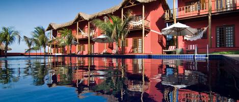 Un resort con piscina, edificios de techo de paja y palmeras.
