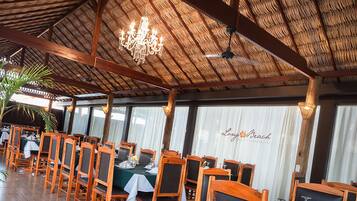 A restaurant with wooden tables and chairs, a thatched roof, and a chandelier.