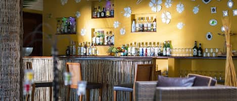 A bar area with a wooden bar counter, shelves with bottles, and a wall decorated with white floral patterns.